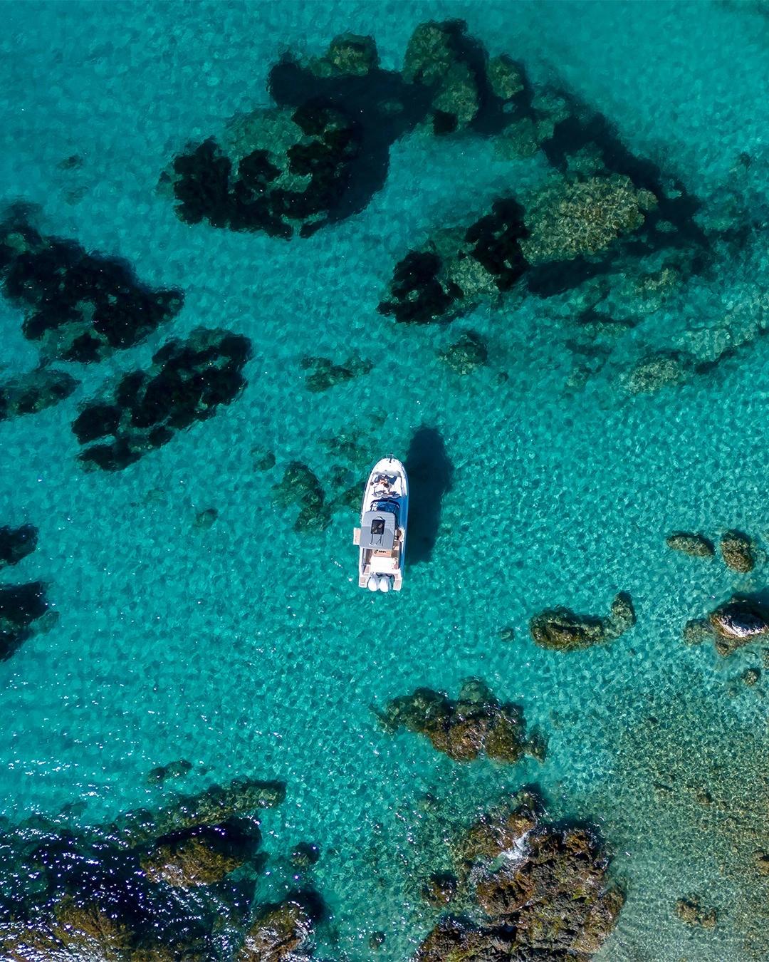 Vue aérienne d'un bateau de plaisance ancré en eaux turquoise près de roches, idéale pour le nautisme et les magasins spécial