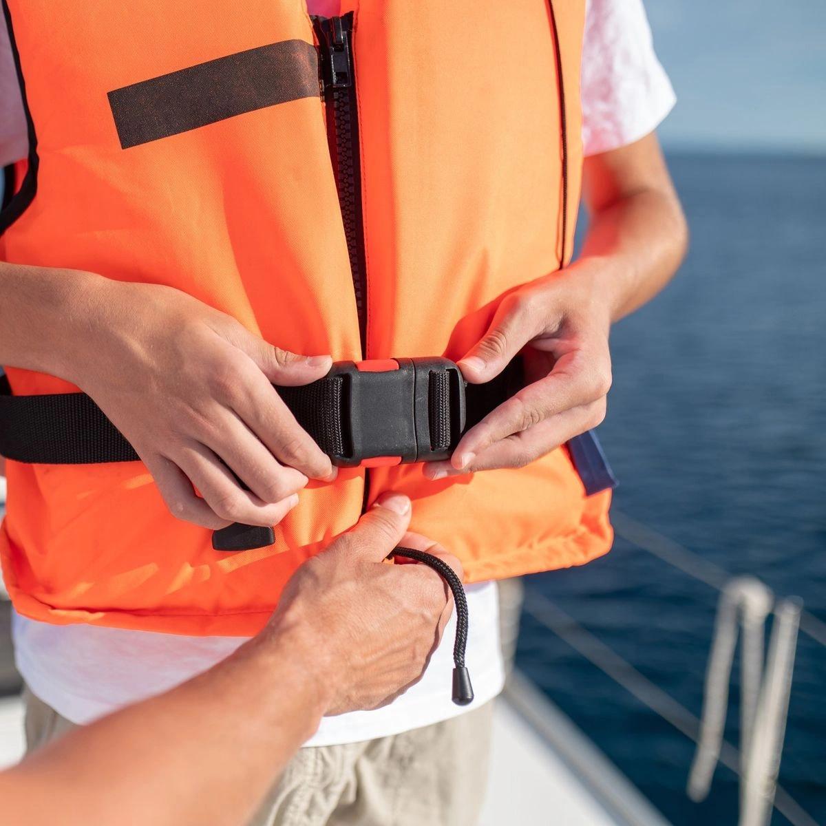 Personne ajustant un gilet de sauvetage orange en magasin nautisme près de la mer