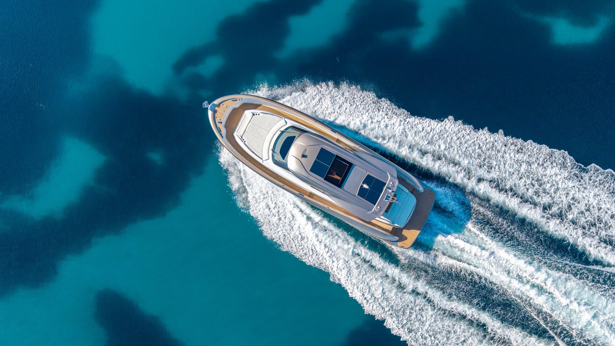 Vue aérienne d'un bateau neuf blanc et bleu naviguant en Corse avec sillages en mer turquoise