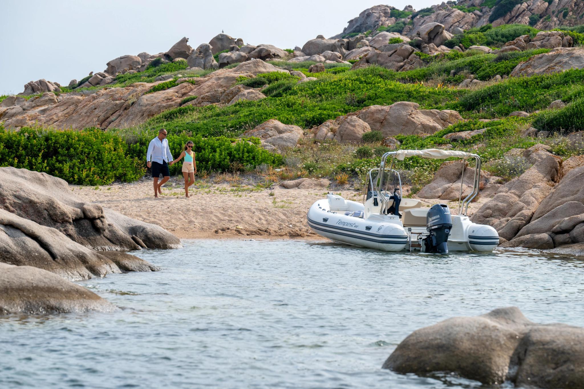 Bateau à moteur amarré en Corse près de rochers granitiques avec deux personnes sur la plage