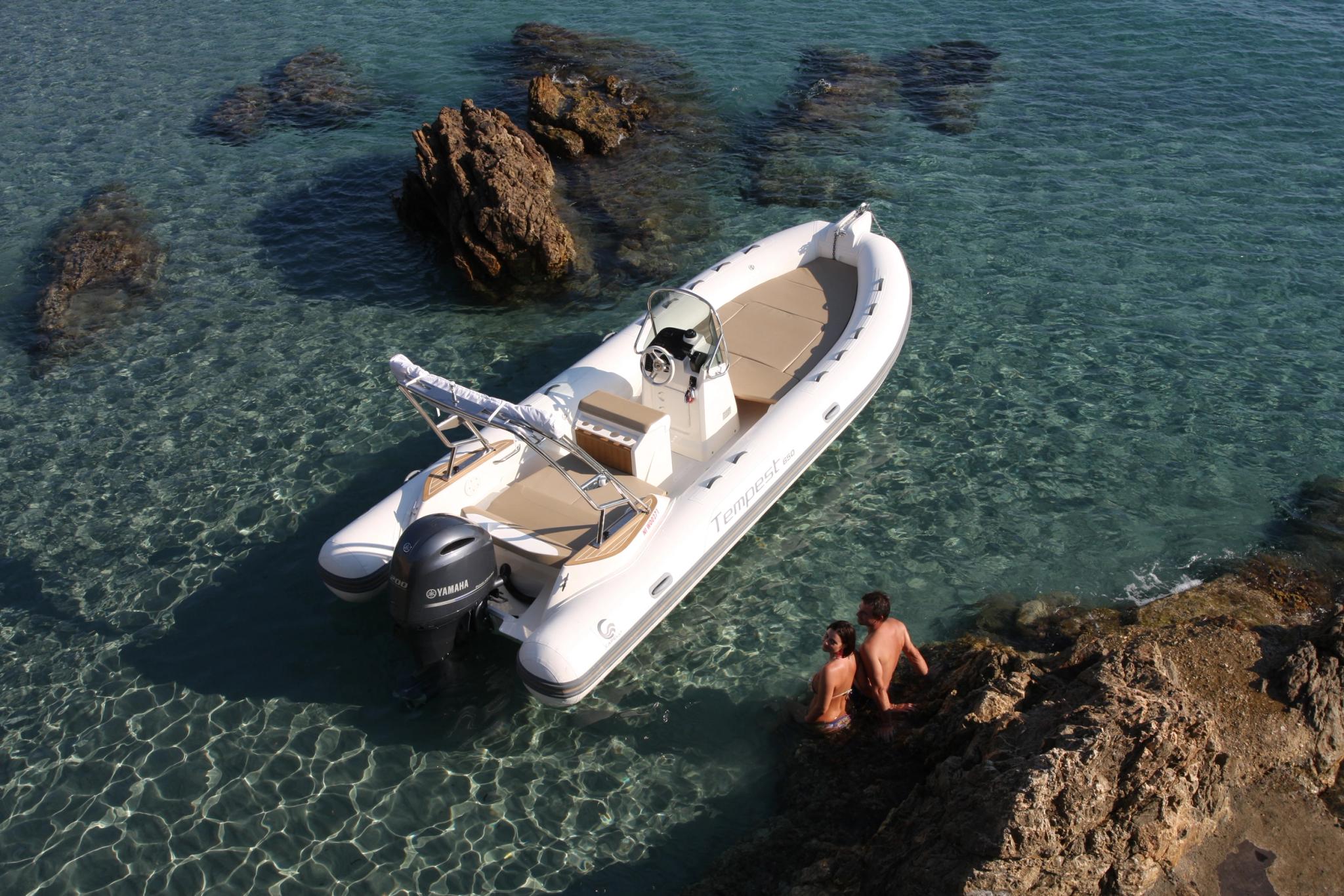 Bateau blanc neuf amarré en Corse avec deux personnes se baignant près des rochers