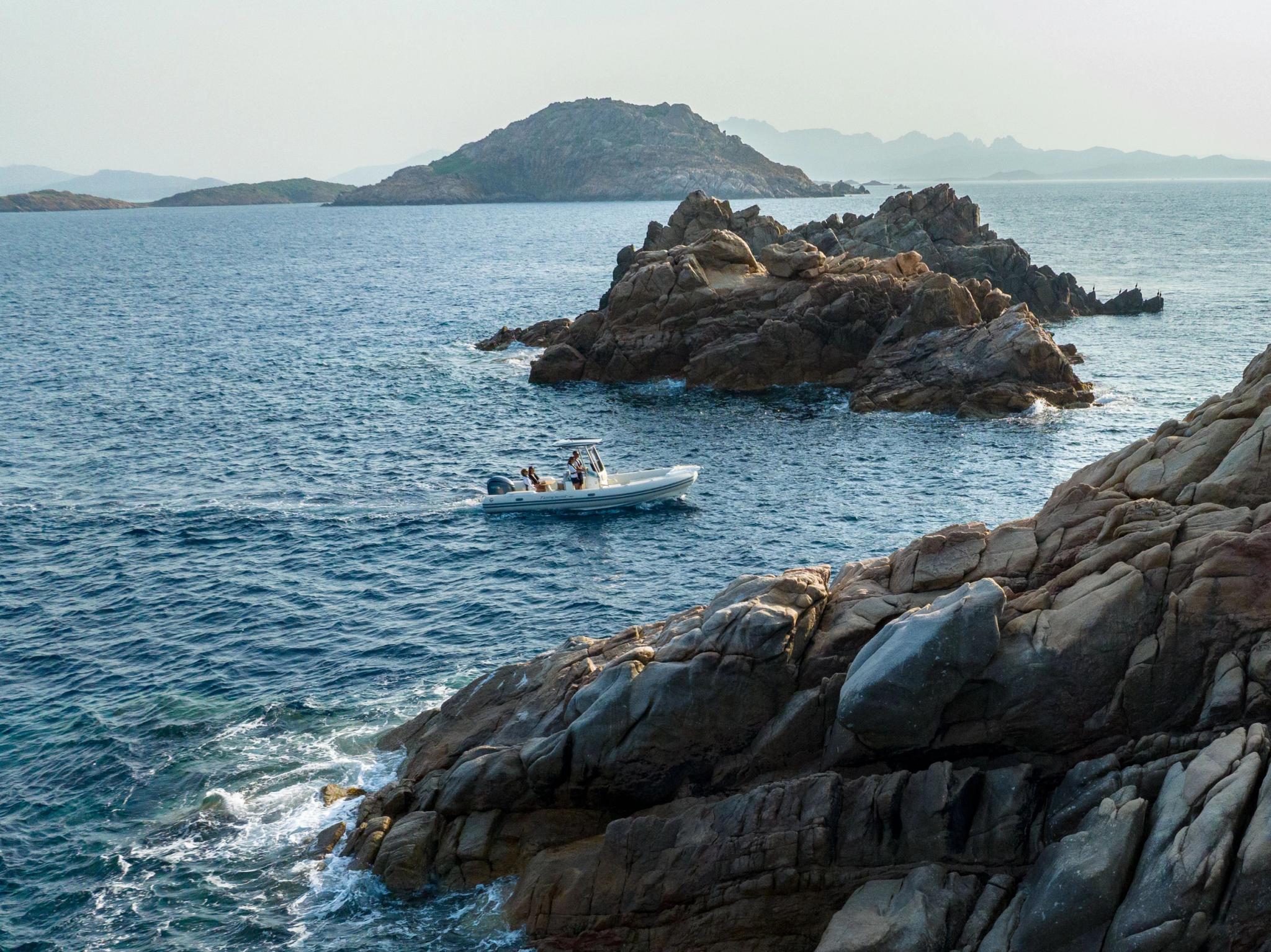 Bateau blanc naviguant près des roches en Corse avec îles en arrière-plan