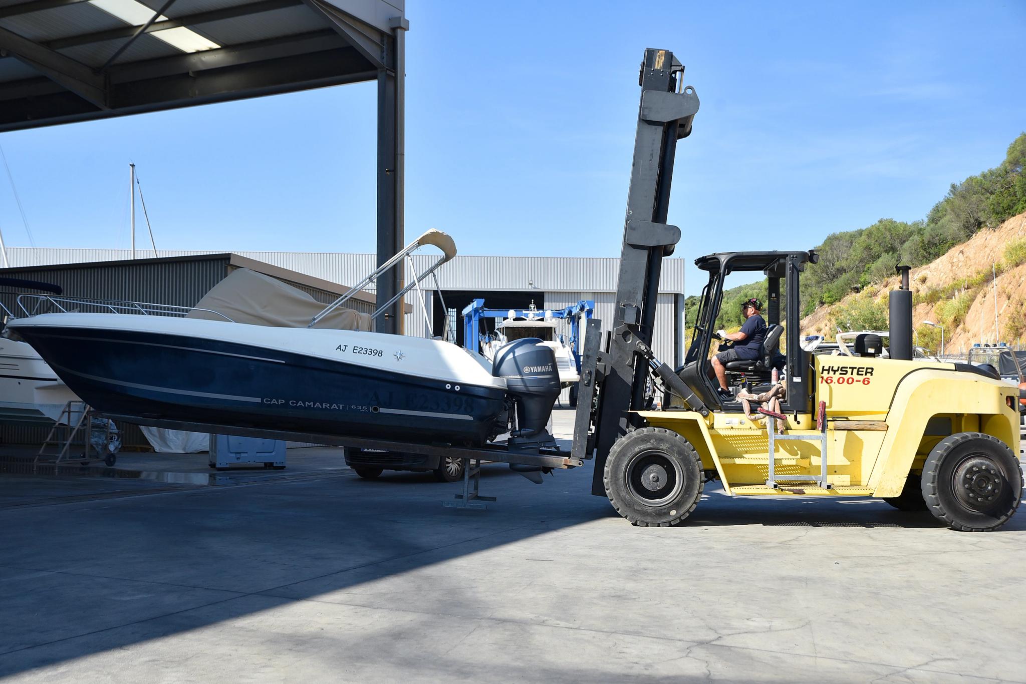 Chariot élévateur jaune Hyster transportant un bateau dans un stationnement couvert