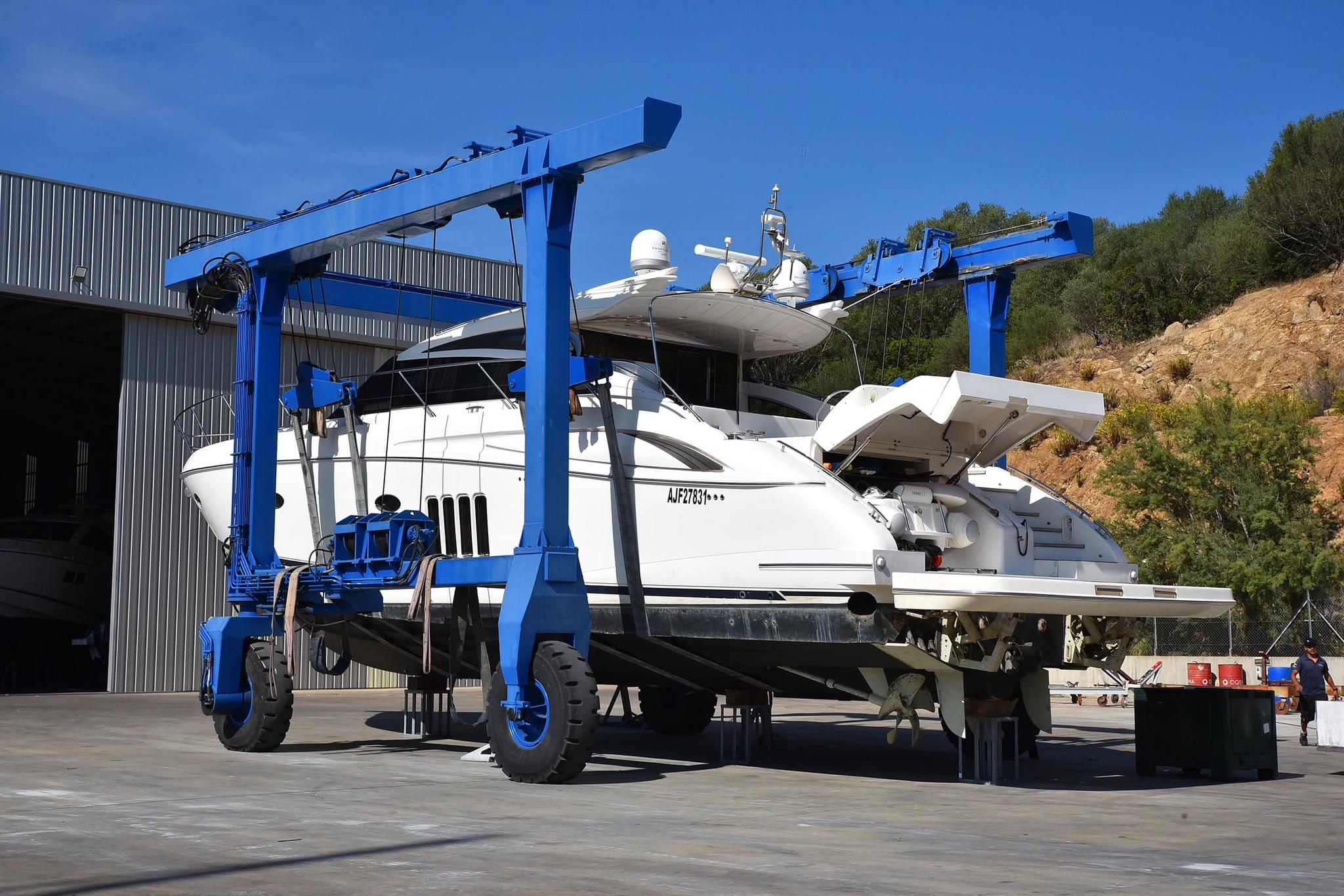 Grue de levage bleue soulevant un bateau blanc pour entretien et réparation de bateaux dans un chantier naval