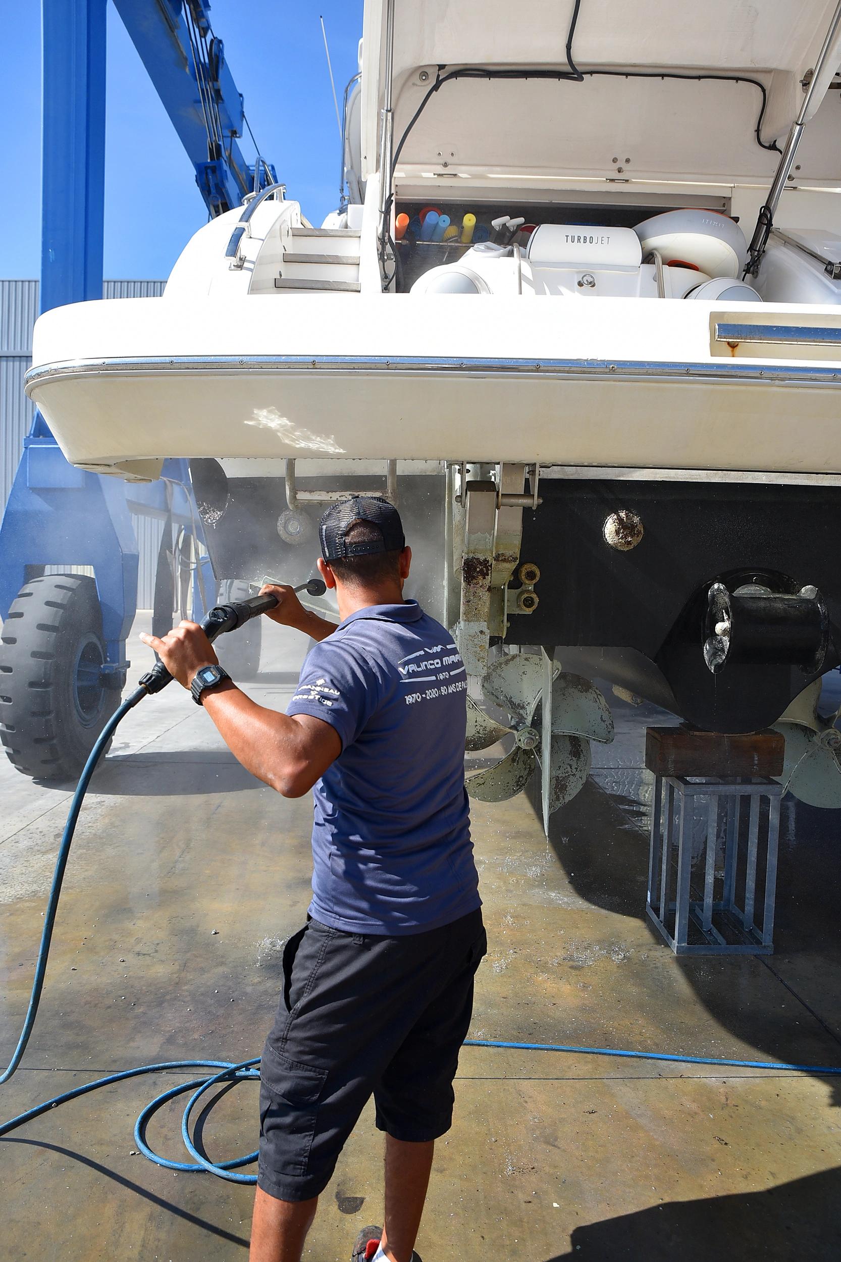 Technicien nettoyant un bateau blanc au chantier naval avec équipement professionnel